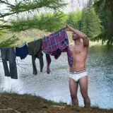 Mann hängt Wäsche auf, darunter auch eine **Boxershorts**, zum Trocknen am Seeufer.