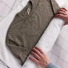 Ein brauner Kaschmirpullover wird auf einem weißen Handtuch gerollt, um ihn nach dem Waschen mit Essig zu trocknen.