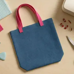 Blauer Beutel mit pinken Henkeln, bereit zum Nähen. Stoffreste, Garn, Schneiderkreide, Schere und Nähclips liegen daneben – ein **beutel schnittmuster**-Projekt.