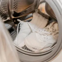 Weiße Sportschuhe in der Trommel einer Waschmaschine, bereit für das Waschprogramm Sport.