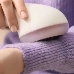 Hand uses a device to remove pilling from a lavender sweater.