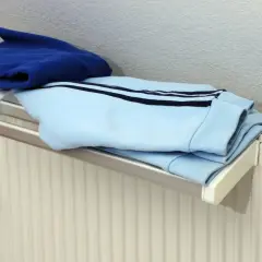 Blaue und hellblaue Kleidung trocknet auf einem Heizkörper. Ein kleiner weißer Kasten mit Display hängt an der Wand.
