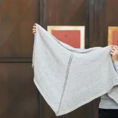 Junge Frau hält ein hellgraues, gestricktes Dreieckstuch hoch.