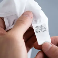 Ein Etikett zeigt Pflegehinweise für ein Kleidungsstück aus Polyester und Baumwolle, inklusive Symbol für einen synthetik waschgang bei 40 Grad.