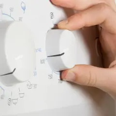 Hand dreht am Regler der Waschmaschine, um einen Kurzprogramm zu wählen.