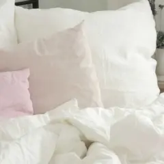 Ein Bett mit weißen und rosafarbenen Leinenkissen. Das Leinen kratzt sanft, lädt zum Entspannen ein.