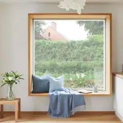 Ein Fensterplatz mit Kissen und Decke lädt zum Verweilen ein. Die Gardinenstange ist dezent gehalten, um den Blick nach draußen nicht zu stören.