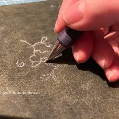 Ein Stift überträgt ein zartes Blumenmuster als Stickmuster auf Stoff.
