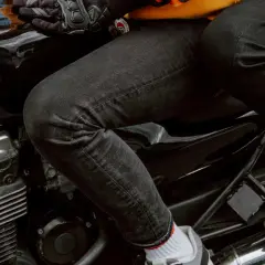 Person sitzt auf einem Motorrad, trägt schwarze Jeans, die frisch gewaschen aussehen, und Motorradhandschuhe.
