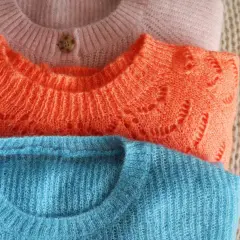 Gestapelte Pullover in Rosa, Orange und Blau. Der Wollprogramm-Waschmaschinen-Zyklus ist ideal für diese feinen Strickwaren.