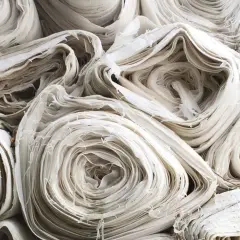 Stapel von weißem, zerknittertem Stoff, der an aufgerollte Papierrollen erinnert. Die Textur ist faserig und unregelmäßig, was auf die Herstellung von Rayonstoff hindeutet, der schädlich für die Umwelt sein kann.