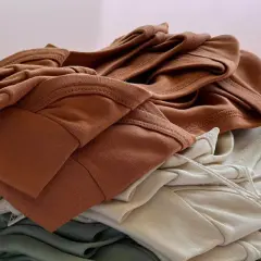 Stapel weicher Stoffe in Erdtönen. Die Falten und Nähte zeigen die Textur, die bei Tencel Nachteile wie Knitteranfälligkeit haben kann.