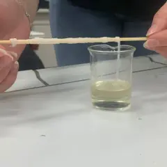 Hände ziehen einen Faden aus einer Flüssigkeit, der zeigt, woraus Nylon besteht.