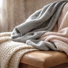 Weiche Decken aus Polyester, die auf einem Stuhl liegen. Staubpartikel tanzen im Sonnenlicht.