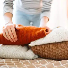 Hände falten gestapelte Pullover aus Wolle und Seide. Sanftes Waschen für die feinen Fasern.