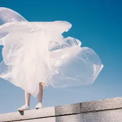 Eine Person steht auf einer Mauer, umgeben von wehendem, weißem Material, das an Plastik erinnert. Polyester schädlich für die Umwelt.