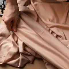 Eine Hand prüft den Stoff einer Viskose Polyester Mischung. Nadeln, Schere und Garn liegen bereit für das Waschen und Nähen.