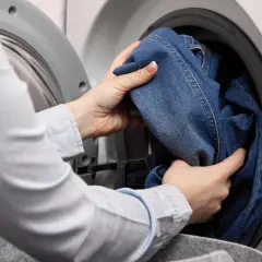 Hände legen Jeans in die Waschmaschine. So kannst du deine Jeans richtig waschen und sie bleiben lange schön.