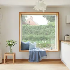Gemütliche Sitzecke am Fenster ohne Fensterbank: Kissen, Decke und Buch laden zum Verweilen ein.