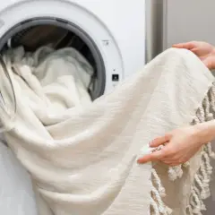 Helle Gardinen werden in die Waschmaschine geladen. Ein Hausmittel wie Backpulver kann helfen, sie wieder strahlend weiß zu machen.