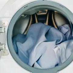 Blaue Kleidung, darunter ein Hemd aus Polyester, wartet im Trommel der Waschmaschine auf den Schleudergang.