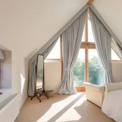 Graue Vorhänge rahmen ein Dreiecksfenster ein und lassen viel Licht herein. Sie sind elegant mit Bändern befestigt.