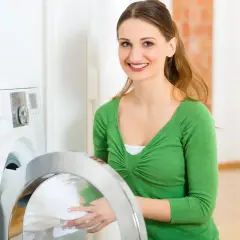 Lächelnde Frau lädt Wäsche in die Waschmaschine. Sie wählt das passende mix programm für ihre Kleidung.