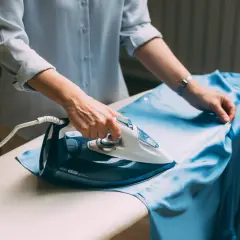 Frau bügelt ein hellblaues Kleid aus knitterfreier Viskose.
