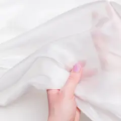 Eine Hand mit lila Nagellack hält ein Stück schimmernde, weiße, fein seide.