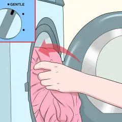 Hand lädt ein rosa Kleid in die Waschmaschine. Das Programm "Sanft" ist eingestellt, um zu verhindern, dass die Viskose eingelaufen ist.