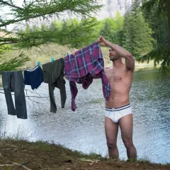 Mann hängt Wäsche auf, darunter auch eine **Boxershorts**, zum Trocknen am Seeufer.