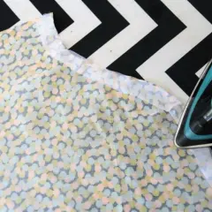 Bügeln eines bunten Stoffes mit einem Bügeleisen. Der Stoff ist mit Kreisen in Pastelltönen bedruckt. Ein Bügeleisen wird verwendet, um eine Kante des Stoffes zu glätten, möglicherweise für eine Viskose-Trockner-Anwendung.