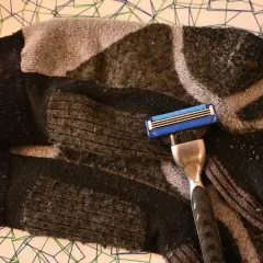 Rasierklinge liegt auf einem stark verknöteltem, gemustertem Schlauch. Pilling hose wird mit der Klinge entfernt.