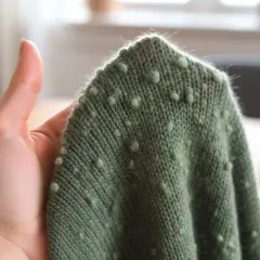 Grüner Strickpullover mit kleinen Noppen, der innen fusselt. Eine Hand hält den Stoff.