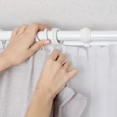 Hände befestigen zwei Gardinen auf einer Stange. Eine Gardine ist grau, die andere weiß und transparent.