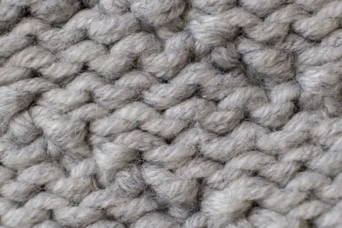 Nahaufnahme einer dicken, grauen Stricktextur. Die Garnstränge sind grob und flauschig, perfekt für einen gemütlichen **Wolle trockner**.
