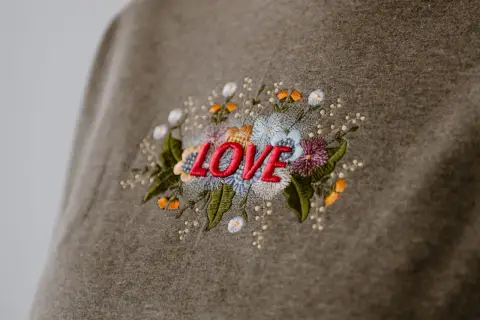 Besticktes Sweatshirt mit dem Wort "LOVE" umgeben von bunten Blumen. Zeigt, was man besticken kann.