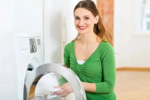 Lächelnde Frau lädt Wäsche in die Waschmaschine. Sie wählt das passende mix programm für ihre Kleidung.