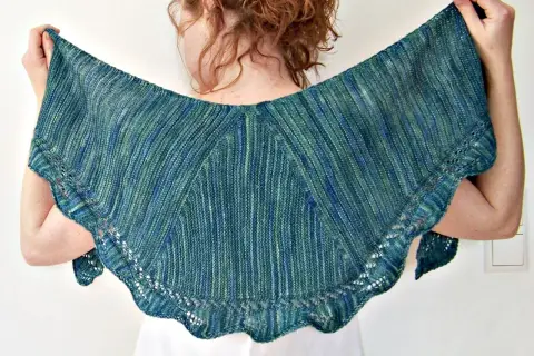 Frau hält ein wunderschönes, blau-grün meliertes **Tuch stricken** mit zarten Lochmustern am Rand.