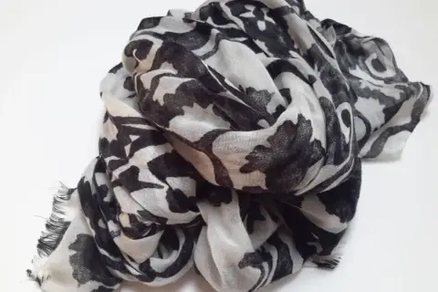 Ein leicht zerknitterter Schal aus Polyester-Plastik mit einem auffälligen schwarz-weißen Blumenmuster.