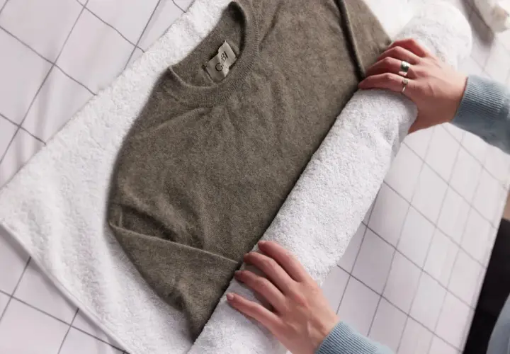 Ein brauner Kaschmirpullover wird auf einem weißen Handtuch gerollt, um ihn nach dem Waschen mit Essig zu trocknen.