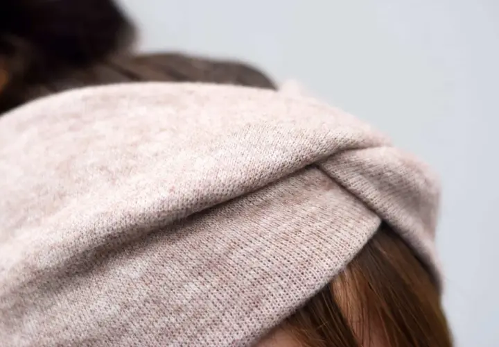 Ein gestricktes Stirnband in Beige mit einem Knoten vorne. Die Breite des Stirnbands ist ideal für einen gemütlichen Look.