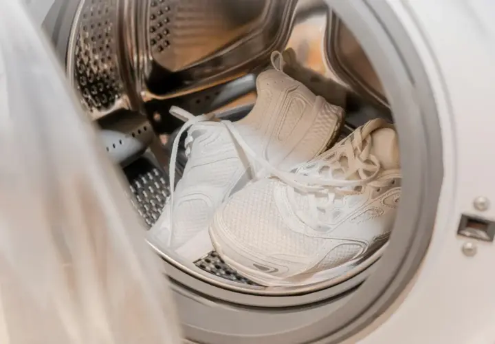 Weiße Sportschuhe in der Trommel einer Waschmaschine, bereit für das Waschprogramm Sport.