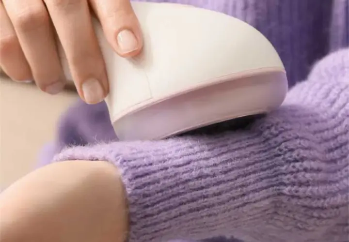 Hand uses a device to remove pilling from a lavender sweater.