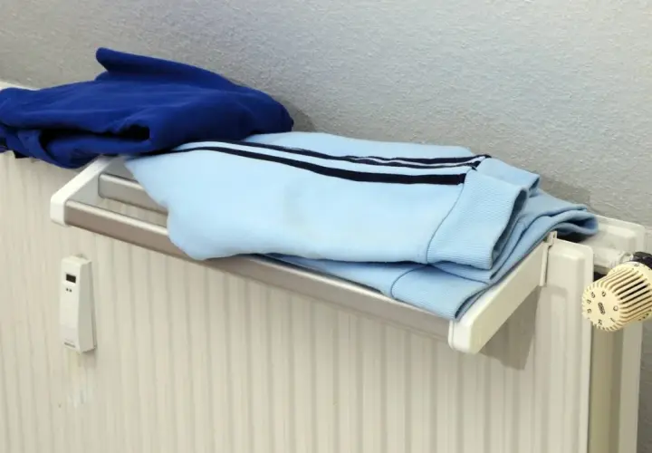 Blaue und hellblaue Kleidung trocknet auf einem Heizkörper. Ein kleiner weißer Kasten mit Display hängt an der Wand.