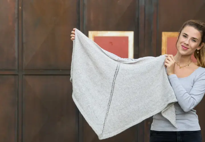 Junge Frau hält ein hellgraues, gestricktes Dreieckstuch hoch.