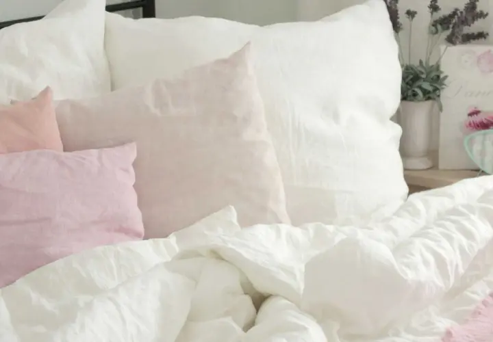 Ein Bett mit weißen und rosafarbenen Leinenkissen. Das Leinen kratzt sanft, lädt zum Entspannen ein.