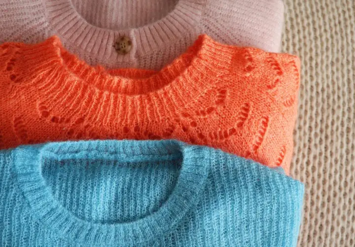 Drei gestapelte Pullover in Rosa, Orange und Blau. Die feine Lammwolle ist bereit für das Waschen, um ihre Weichheit zu erhalten.