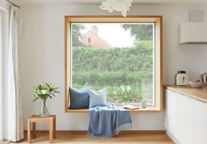 Ein Fensterplatz mit Kissen und Decke lädt zum Verweilen ein. Die Gardinenstange ist dezent gehalten, um den Blick nach draußen nicht zu stören.