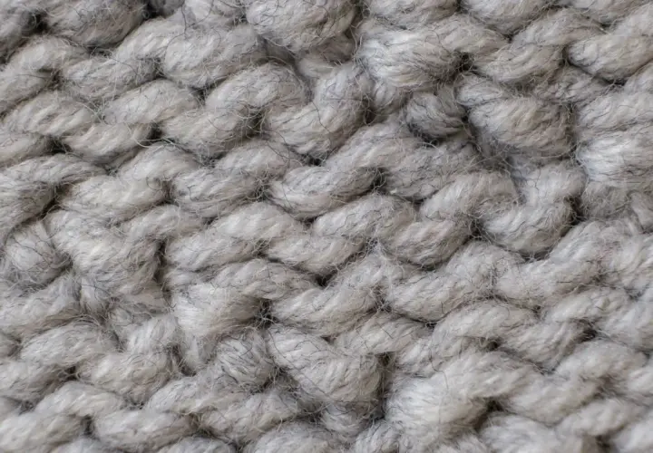 Nahaufnahme einer dicken, grauen Stricktextur. Die Garnstränge sind grob und flauschig, perfekt für einen gemütlichen **Wolle trockner**.